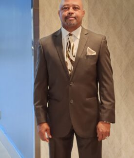 A man in a suit and tie standing next to a wall.